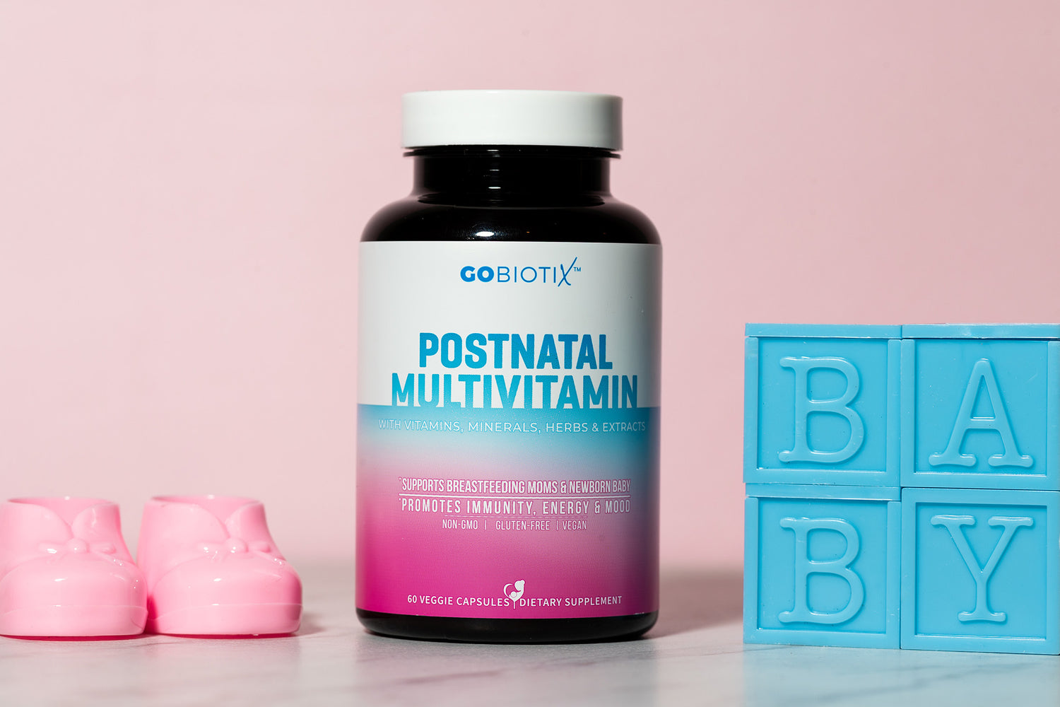 Gobiotix Postnatal Multivitamin bottle with pink baby shoes and blue 'BABY' block on a pink background
